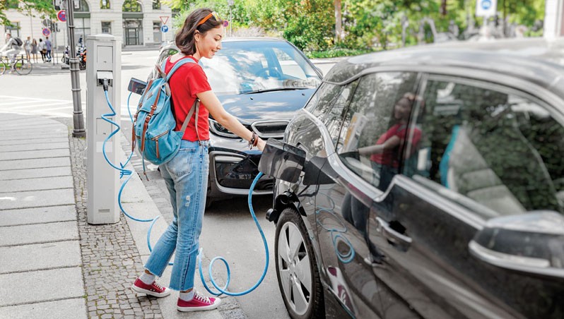 Woman charging her electro car at special parking, alternative energy and eco concept